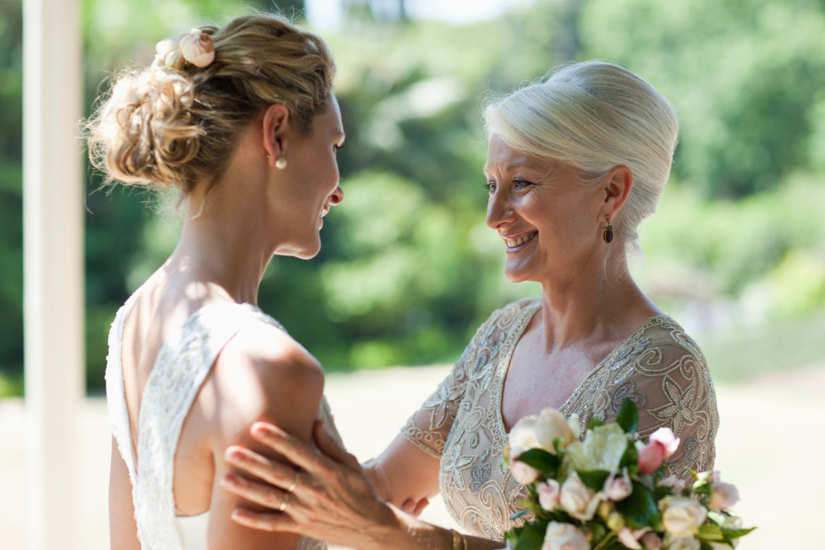 A bride in a white lace wedding dress sharing a joyful moment with her mother in a beige lace top on her wedding day.