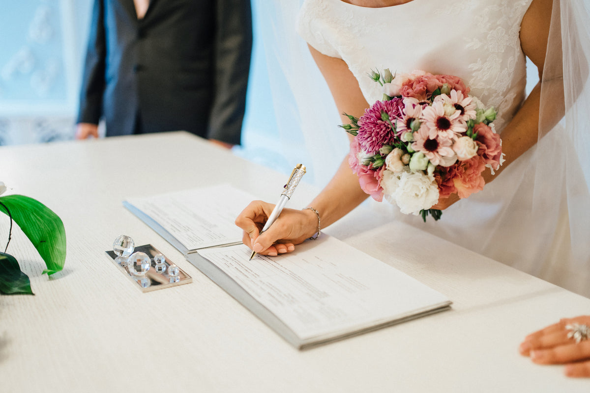 A bride in a white wedding dress signing her wedding documents with the Wedding Pen.